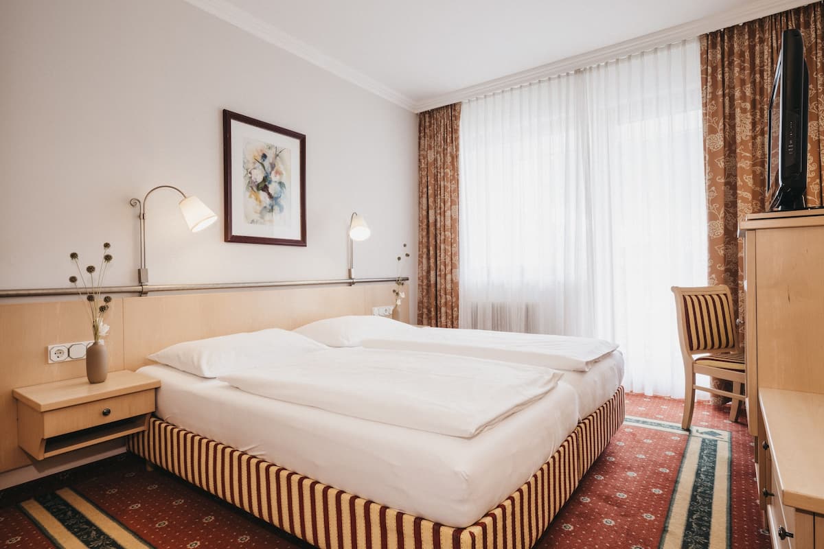 A hotel room with two beds, a desk, a chair, a lamp, and a painting on the wall.