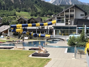 A pool area with a water slide, lounge chairs, and a view of mountains. - Sporthotel Royer (Schladming)