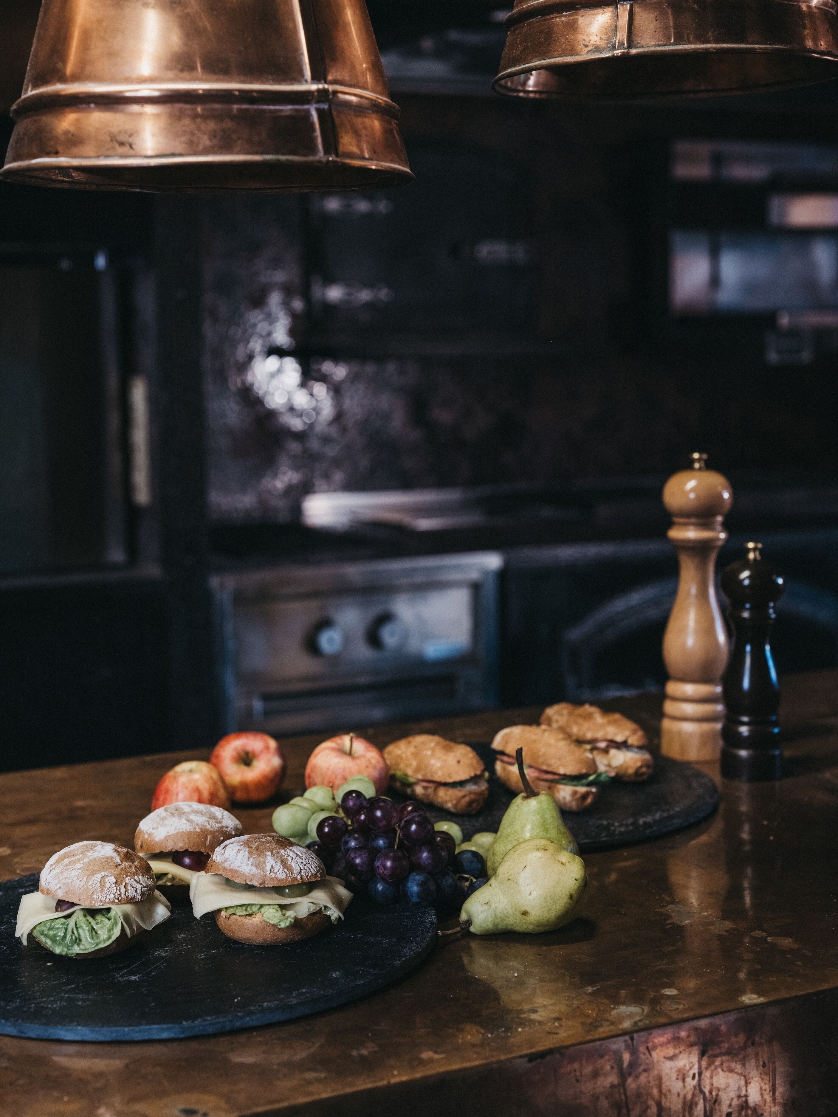 A kitchen counter with a variety of food items including sandwiches, apples, grapes, and pears.