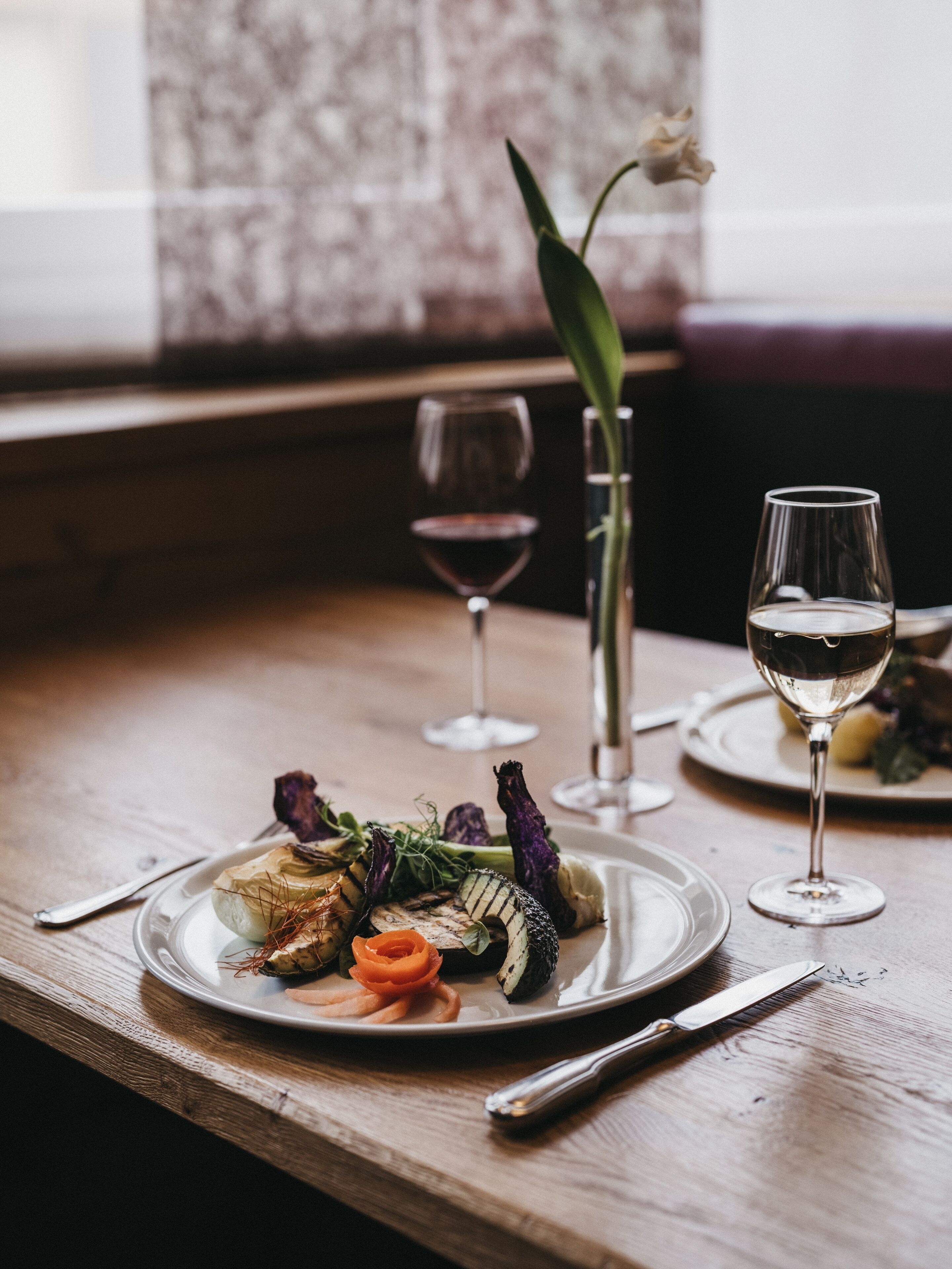 A dining table with plates of food, wine glasses, and cutlery.