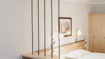 A hotel room with a bed, a desk, a chair, a wardrobe, and a painting on the wall.