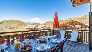 Une terrasse en bois avec une table dressée pour le petit-déjeuner, offrant une vue sur un paysage montagneux.