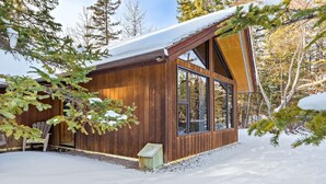 Eine Holzhütte mit großen Fenstern und einem geneigten Dach, umgeben von Schnee und Bäumen.