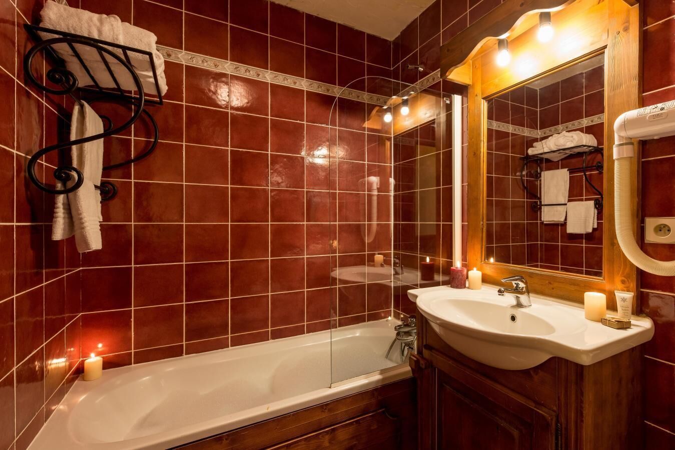 A bathroom with a bathtub, a sink, and a mirror. There are towels hanging on a rack and candles on the floor.