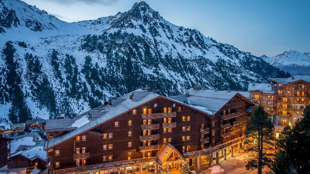 Ein mehrstöckiges Chalet mit Balkonen und einer Skipiste im Hintergrund.