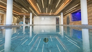 En rymlig inomhuspool med modern design, med ett träpanelat tak och en skylt med texten ”CHALLET ALTITUDE”.