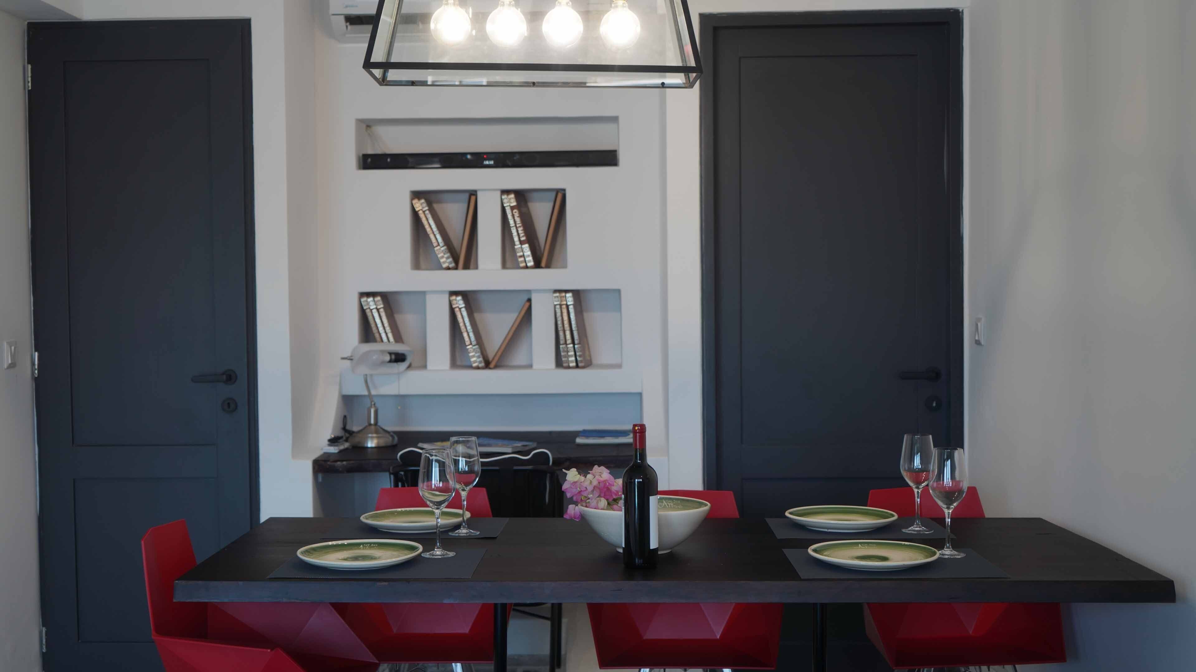 Een eethoek met een tafel voor twee personen, rode stoelen, een hanglamp en boekenkasten erboven.