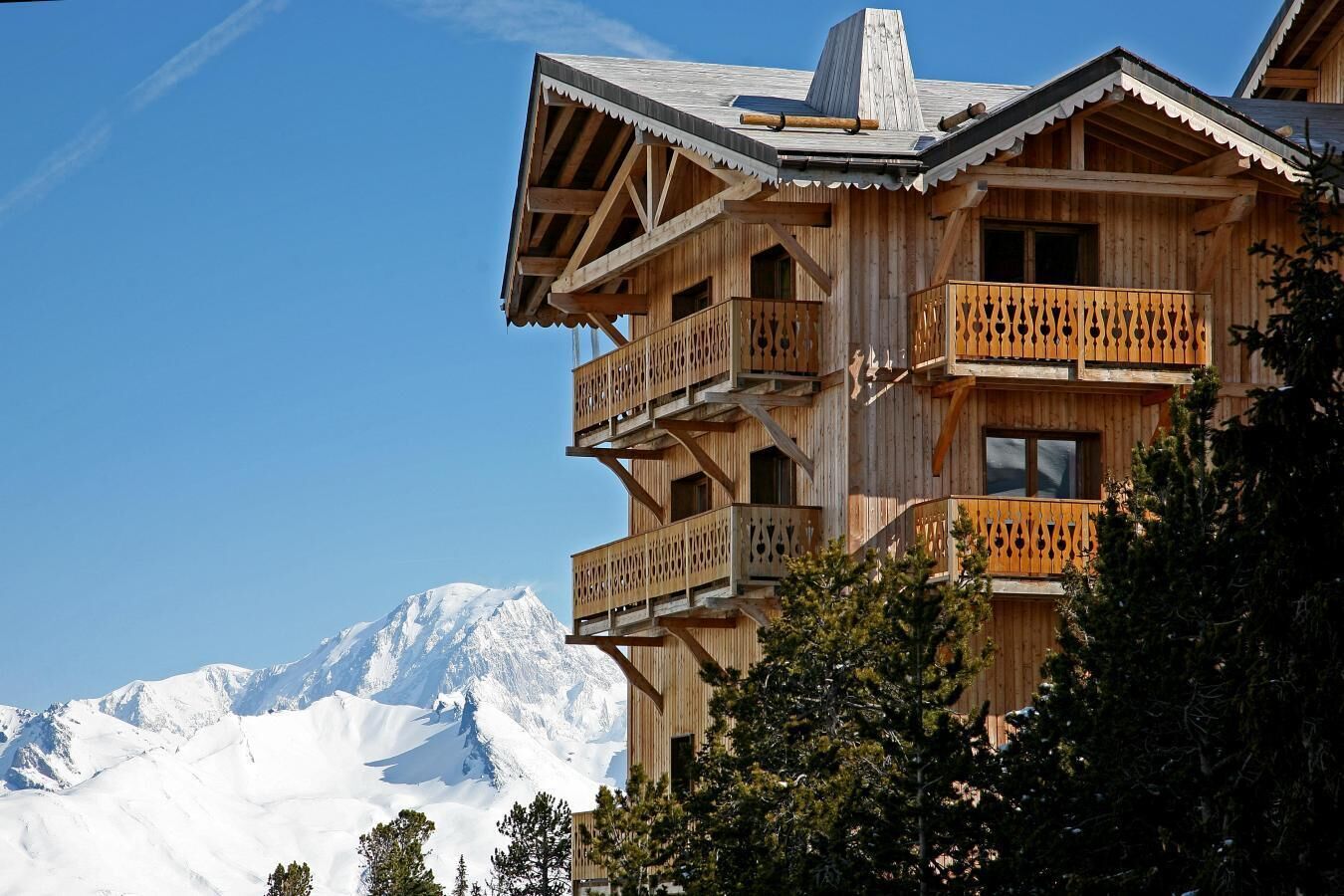 Una cabaña de madera con varios balcones y vistas a montañas nevadas.