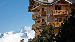 Un chalet en bois doté de plusieurs balcons et offrant une vue sur des montagnes enneigées.