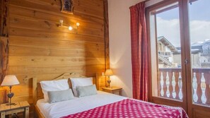 A wooden-paneled bedroom with a bed, two bedside tables, a window with a view of buildings, and a balcony with a railing. - Chalet, sauna, terrace, fireplace or stove, parking, tv, ski locker, 110m² (Saint-Martin-de-Belleville)