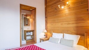 A bedroom with a wooden headboard, a bed with white bedding, a nightstand with a lamp, and a bathroom visible through an open door. - Chalet, sauna, terrace, fireplace or stove, parking, tv, ski locker, 110m² (Saint-Martin-de-Belleville)