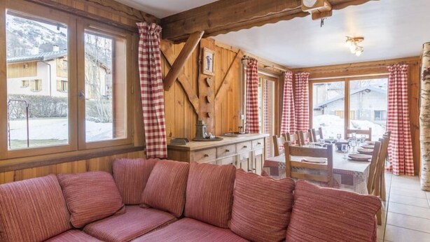 A cozy room with a wooden ceiling, a sofa, a dining table set for four, and large windows with checkered curtains. - Chalet, sauna, terrace, fireplace or stove, parking, tv, ski locker, 110m² (Saint-Martin-de-Belleville)