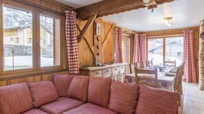A cozy room with a wooden ceiling, a sofa, a dining table set for four, and large windows with checkered curtains. - Chalet, sauna, terrace, fireplace or stove, parking, tv, ski locker, 110m² (Saint-Martin-de-Belleville)