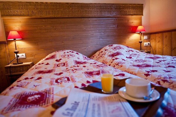 A hotel room with two beds, wooden headboard, two bedside lamps, a breakfast tray with a cup and orange juice, and a newspaper.