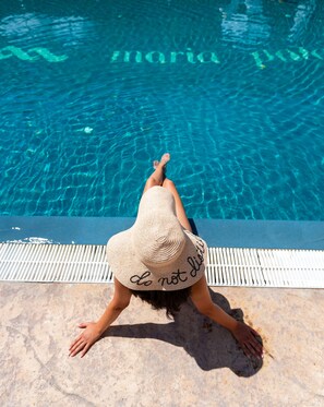 Una persona con sombrero de paja sentada junto a una piscina, donde se lee la advertencia: “No saltar”.