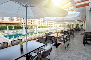 An outdoor dining area with tables and chairs, a pool, and umbrellas.