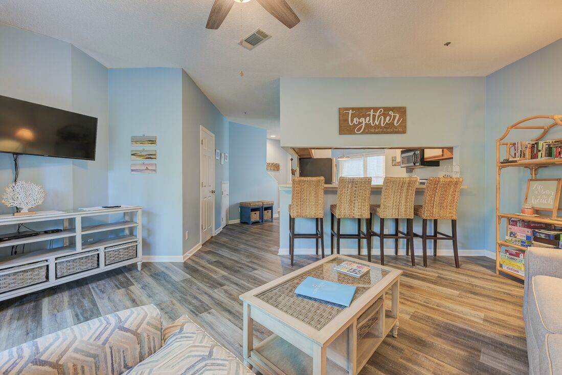 A living room with a TV, a coffee table, and a bar area with wicker chairs.