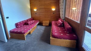 Ein Zimmer mit zwei hölzernen Betten, roter Bettwäsche, einer Holzwand und zwei Wandleuchten.