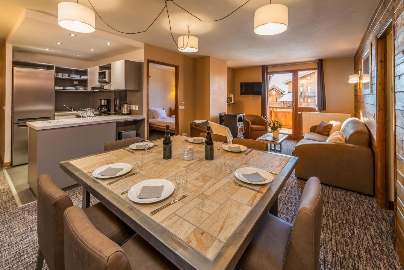 A modern kitchen with a central island, dining area with a table set for four, and a cozy living area with a sofa and a TV.