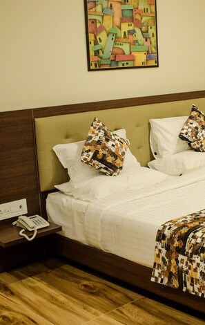 A hotel room with a wooden headboard, a bed with white linens, two patterned pillows, a bedside table with a phone, and a colorful painting on the wall. - Millennials Hotel (Anekal)