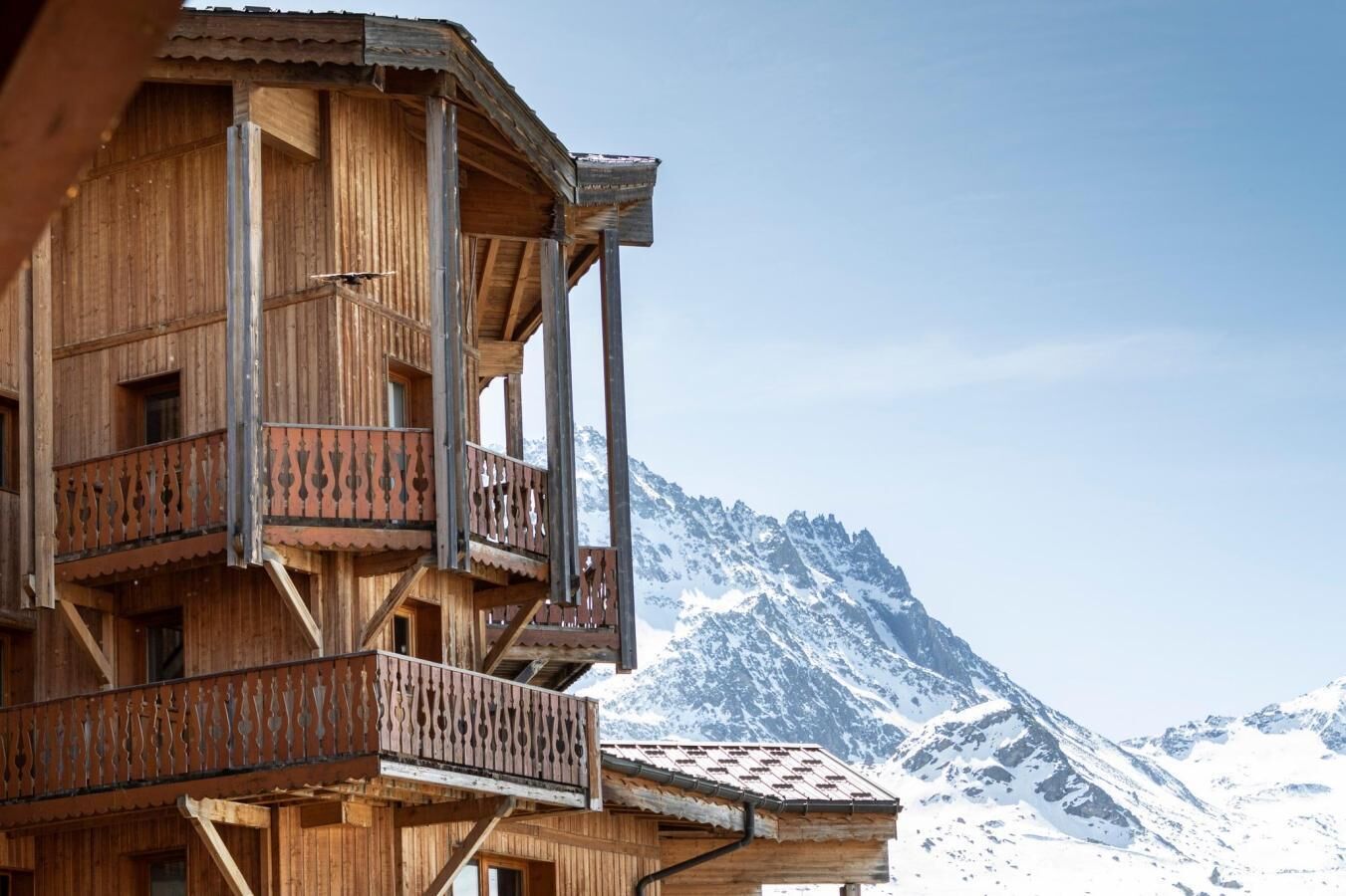 A wooden chalet with multiple balconies, set against a backdrop of snow-covered mountains.