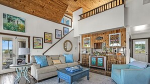 A spacious living room with a high ceiling, a staircase, a kitchen area, and a dining area.