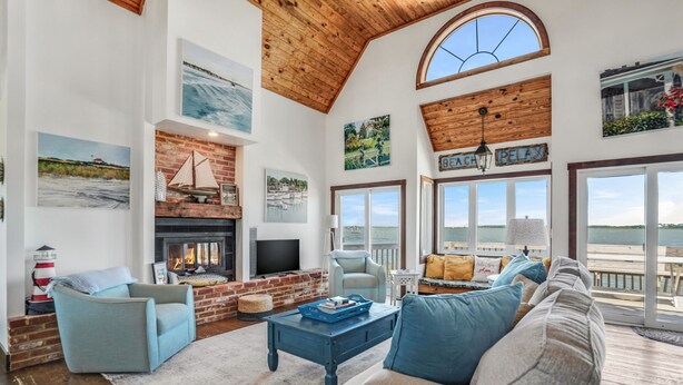 A spacious living room with a fireplace, comfortable seating, and large windows offering a view of the outdoors.