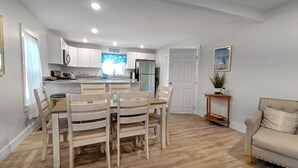 Une cuisine moderne avec des meubles blancs, un îlot central et un coin repas doté de chaises en bois.