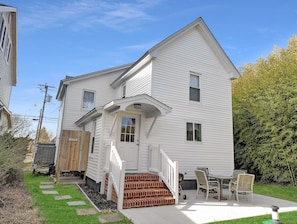Ein zweistöckiges Haus mit Veranda, einer Treppe zum Eingang und einer Terrasse mit Gartenmöbeln.