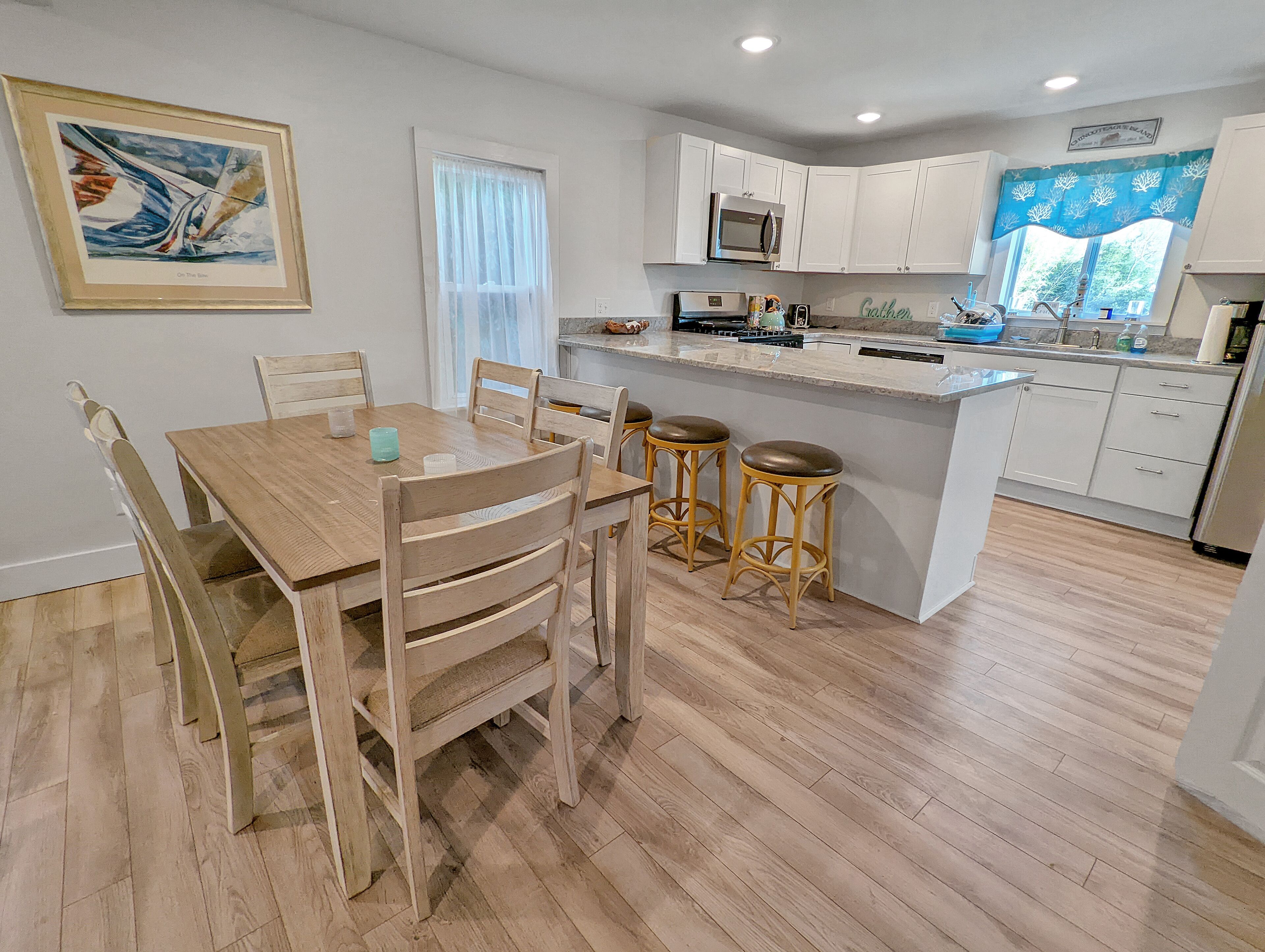 A modern kitchen with white cabinets, a wooden dining table, and bar stools.