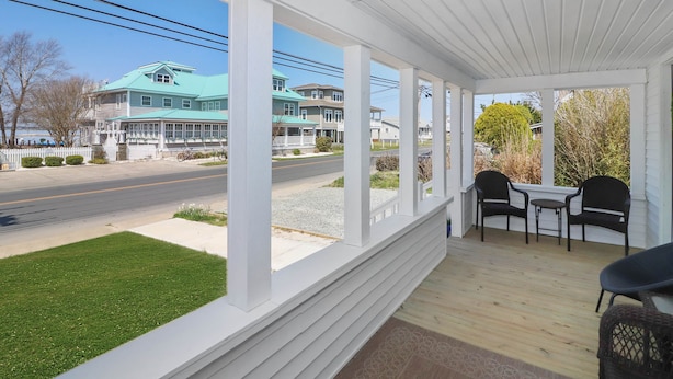 Une véranda couverte avec des balustrades blanches, une terrasse en bois et deux tables accompagnées de chaises.
