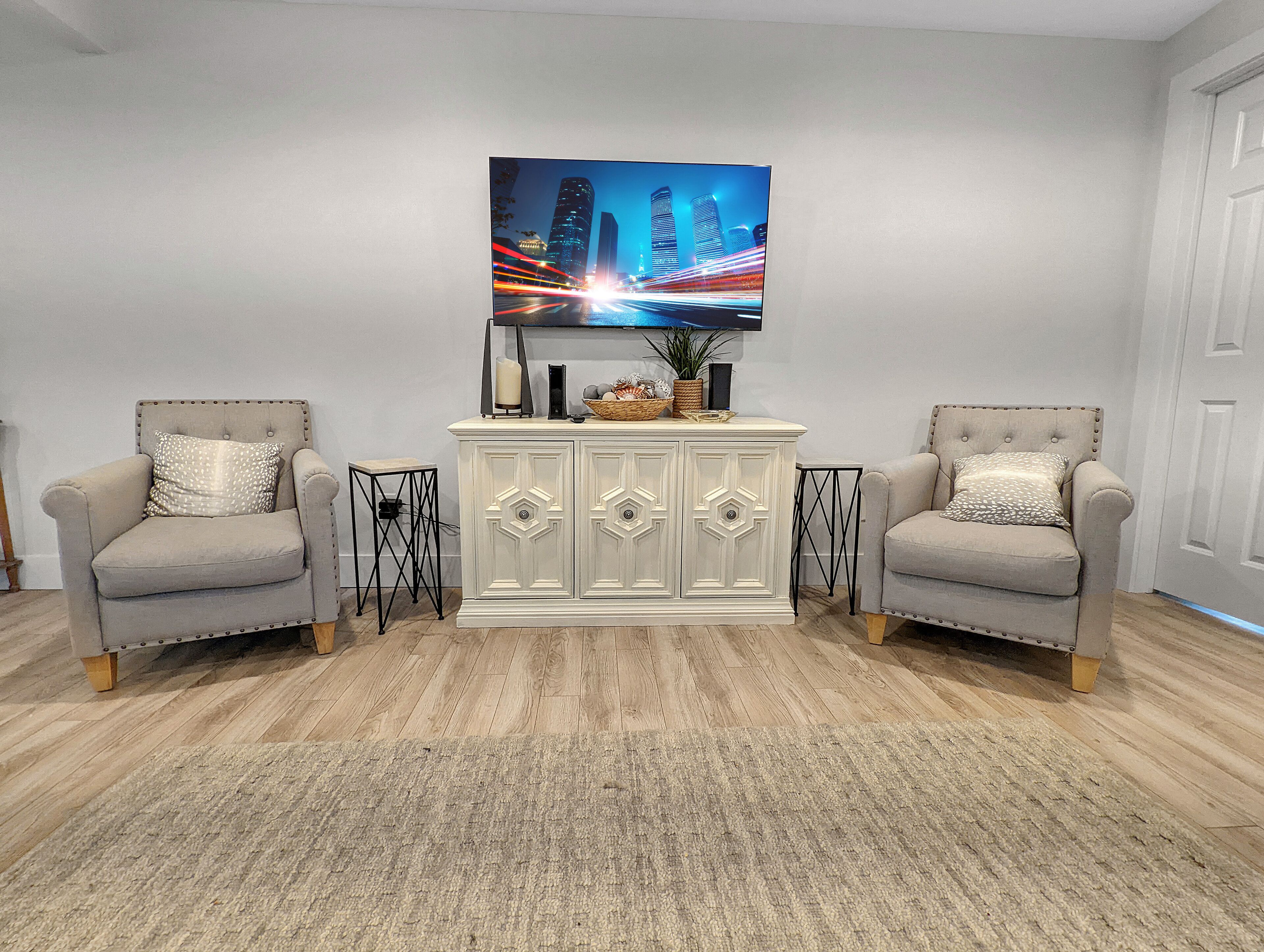 Een zithoek met twee fauteuils, een wit kastje en een stadsgezichtschilderij aan de muur.