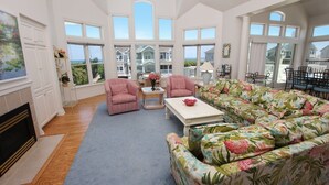 Ein geräumiges Wohnzimmer mit großen Fenstern, einem Kamin und einem blumigen Sofa.