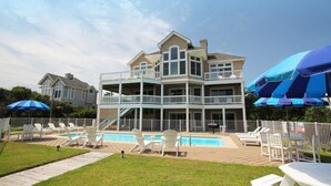 Ein zweistöckiges Gebäude mit Pool, Außenbereich zum Sitzen und einem umzäunten Deck.