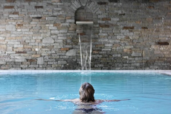 A person swimming in a pool with a stone wall in the background.