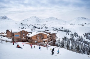A ski resort with wooden buildings, ski slopes, and snow-covered mountains.