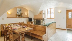 Un coin repas avec une table et des bancs en bois, une cheminée en pierre et un téléviseur posé sur un meuble.
