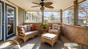 Eine überdachte Veranda mit Korbmöbeln, einem Deckenventilator und Blick auf die Nachbarhäuser.