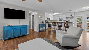 Ein geräumiges Wohnzimmer mit Flachbildfernseher, einem blauen Schrank, einem weißen Sofa und einem Holzkühlventilator.