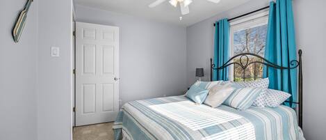 Ein Schlafzimmer mit Bett, Deckenventilator, Fenster mit Vorhängen und einer Tür.