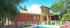 Ein Schwimmbecken mit Liegestühlen, ein Gebäude mit einem Ziegeldach und ein Logo mit einer Hausumrisszeichnung und dem Text "villas Orinella".