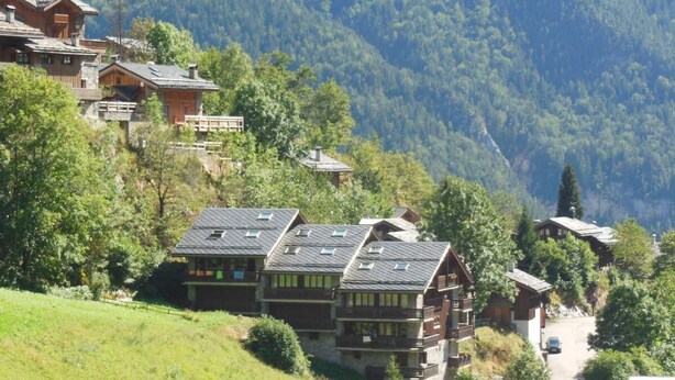 A cluster of wooden cabins with multiple stories and balconies, surrounded by lush greenery and mountains in the background. - 2nd floor, view village, balcony, tv, ski locker, 75m², Champagny-en-Vanoise (Champagny-en-Vanoise)