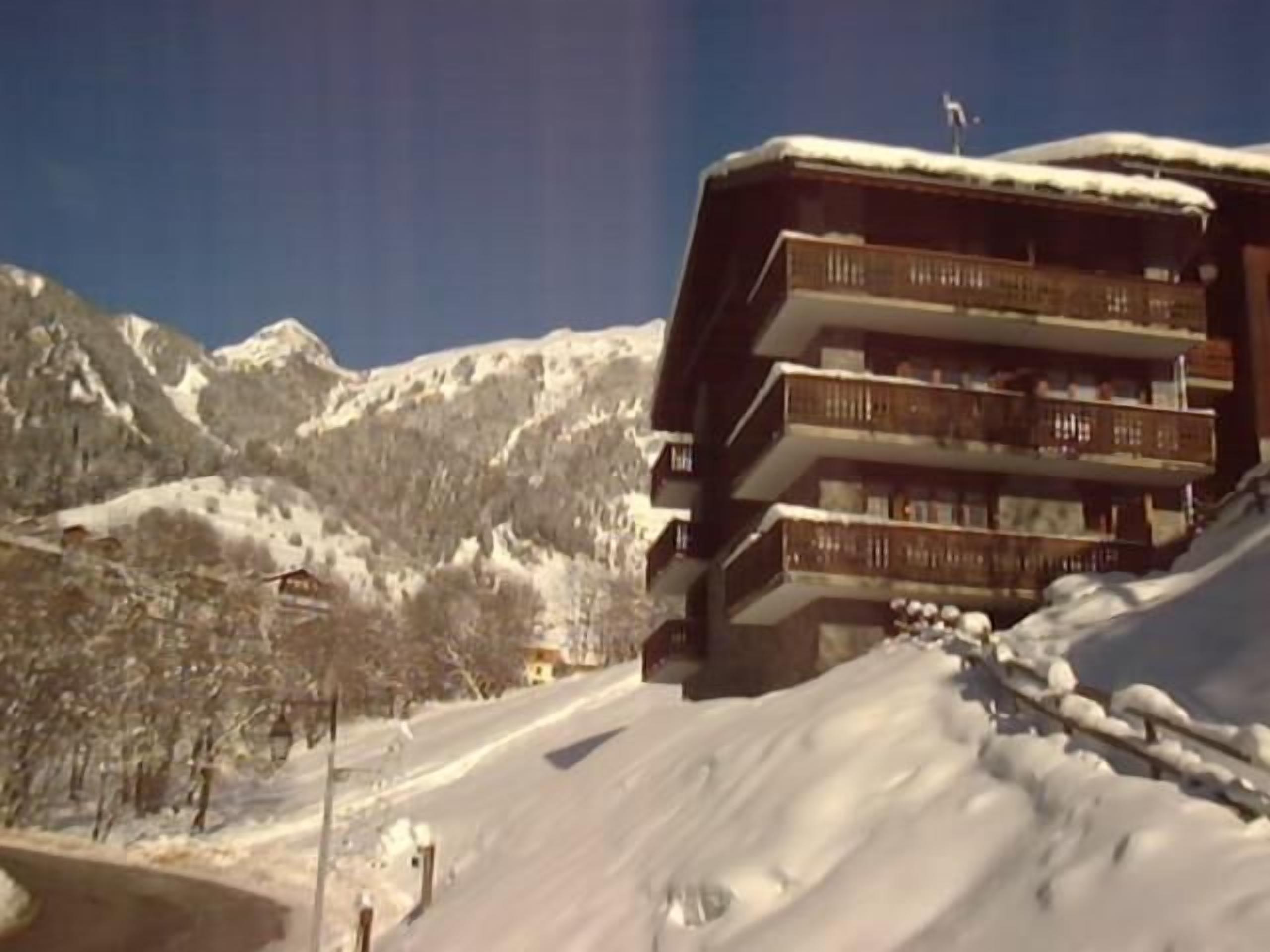 A multi-story building with balconies, surrounded by snow-covered mountains.