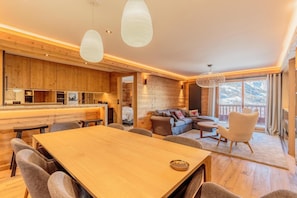A modern interior with a wooden dining area, a sofa, and a balcony with a mountain view.