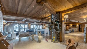 A spacious living area with a high ceiling, wooden beams, a fireplace, and a cozy seating arrangement. - 200m from resort center, 3rd floor, view mountain, fitness, swimming pool, sauna, hammam, balcony (Saint-Martin-de-Belleville)