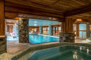 An indoor swimming pool with stone pillars, lounge chairs, and a view of the outside.
