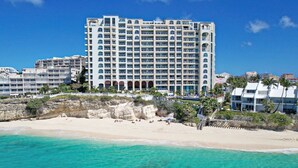 Ein Strandhotel mit mehreren Etagen, Balkonen und einem Sandstrand im Vordergrund.