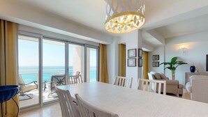 Ein geräumiges Zimmer mit großem Esstisch, einer Couch und einem Balkon mit Meerblick.