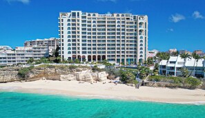 A beachfront hotel with multiple floors, balconies, and a sandy beach in the foreground.