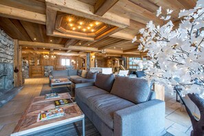 A cozy log cabin interior with a large gray sofa, a coffee table with magazines, and a fireplace.